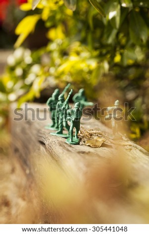 Green plastic toy soldier army unit walking on top of an old weathered railway sleeper. Selective focus and wooden textured background