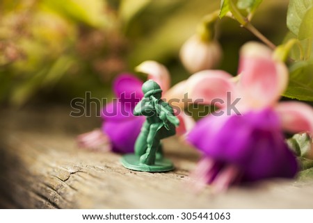 Green plastic toy soldier army sniper on top of an old weathered railway sleeper. Selective focus and wooden textured background and purple flowers