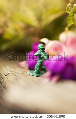 Green plastic toy soldier army sniper on top of an old weathered railway sleeper. Selective focus and wooden textured background and purple flowers