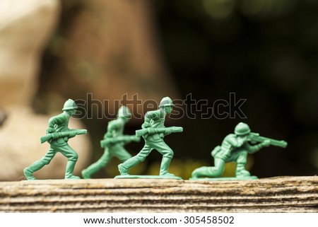 Green plastic toy soldier army unit running on top of an old weathered railway sleeper. Selective focus and wooden textured background