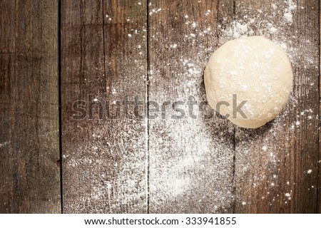 Ball of pizza dough on a rustic wooden background with dusting of flour
