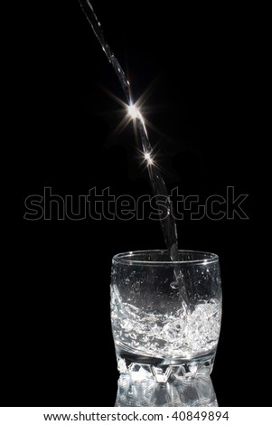 Glas with water on black Background. Water drops from the top to glass