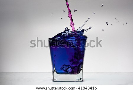 Water splash in a glass with colour water on white backgroung. Pink and blue.
