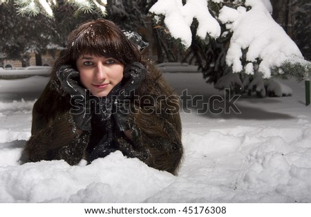 Portrait of beautiful female laying on snow under evergreen trees covered with snow in winter park