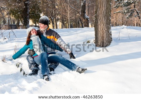Happy, young couple is smiling while sitting at the snow. Embracing an looking to each other
