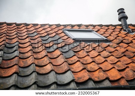 A window in the roof with red tiles and chimney