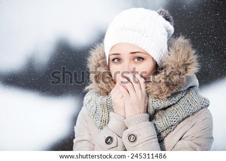 Cold snap in the streets. Snowfall in the streets. Portrait of a girl heating hands with his breath.