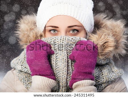 Portrait of a beautiful girl in a scarf and gloves in winter park. flying snow