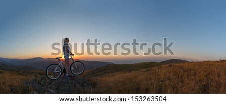 Young slim lady standing on top of a mountain with bicycle and enjoying valley view