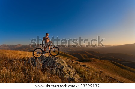 Young slim lady standing on top of a mountain with bicycle
