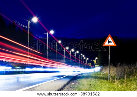 Danger sign by the road at night with cars passing by