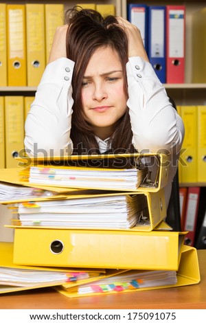 Young secretary distressed with a lot of documents on her desk