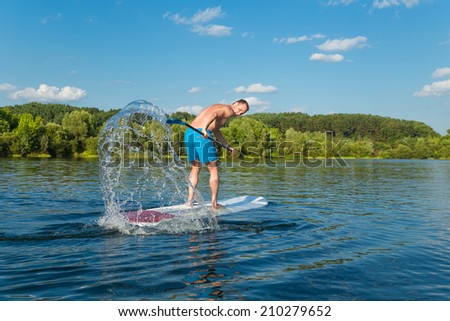Young attractive man splashing water on stand up paddle board in the lake, SUP