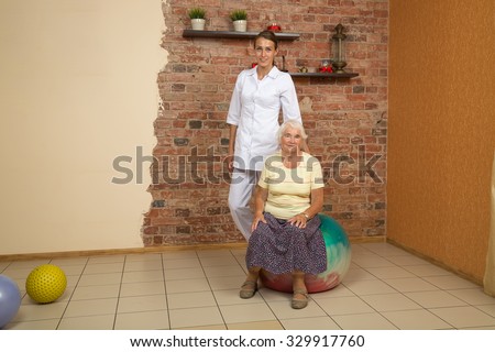 Senior Woman Sitting On A Gym Ball During Physiotherapy, Looking At Camera