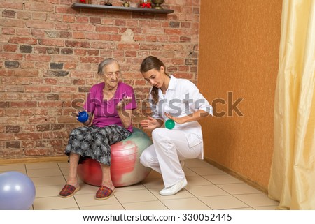 Senior Woman Sitting On A Gym Ball And Doing Exercise With Physical Therapist