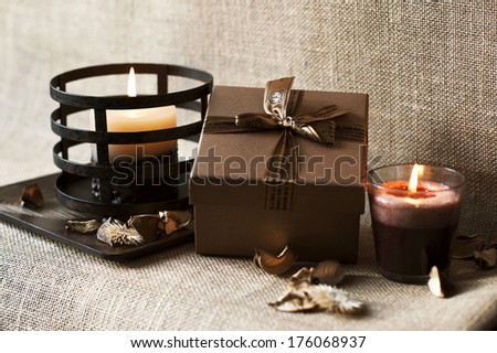 Golden-brown gift box with candles on wooden plate. Burlap/sack background