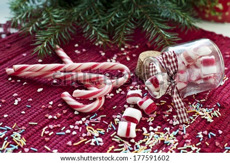 Spilled/poured from glass jar sweet candies with red and white candy cane on red christmas background