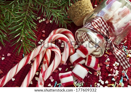 Spilled/poured from glass jar sweet candies with red and white candy cane on red christmas background