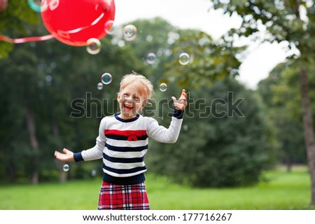 Emotional laughing  little blonde girl playing/catching soap bubbles in the green summer park.