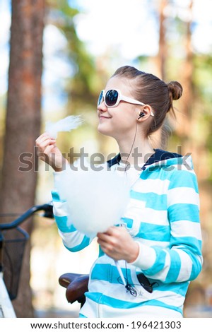 Smiling happy girl in sportswear in spring park eating cotton candy. Child treat. Outdoors.