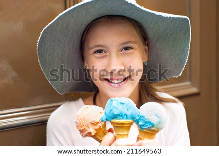 Happy beautiful smiling girl in summer hat holding many colored round ice-cream. Outdoors.