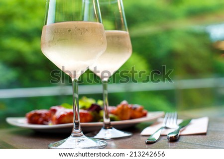 Table setting with two glasses of delicious cooled white wine with snack on background. Summer close-up.