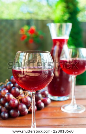 Two glasses and carafe of delicious homemade red wine with grape on wooden table. Outdoors still-life.