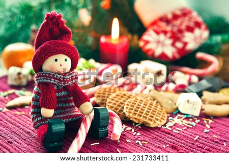Wooden smiling doll with sweet striped candy canes on christmas background. New-year\'s indoor still-life. Close-up.