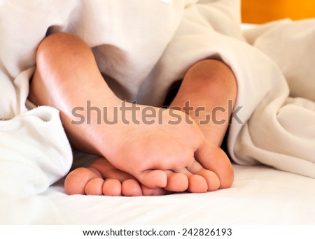 Sleeping child dirty feet on white bed linen from backside. Indoors close-up.