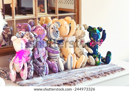 Many textile tilda teddy bear toys sitting in a row in workshop. Indoors.
