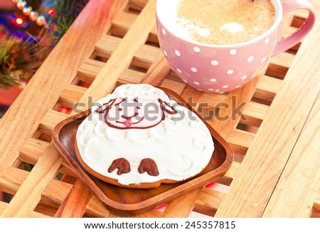 Sheep shape gingerbread and cup of milk with cinnamon sticks on christmas background. Festive indoors closeup.