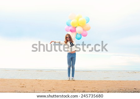 Funny smiling happy girl with many colored air balloons on the seaside. Outdoors. Filtered image.