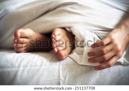 Sleeping little child feet and hand on white bed linen. Indoors closeup.