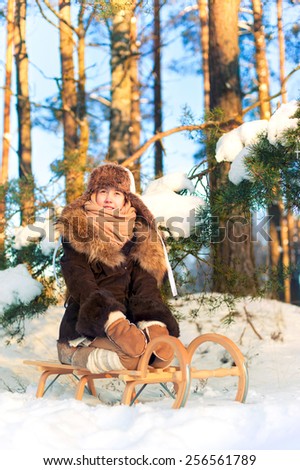 Beautiful cheerful little girl sitting on sledges in winter forest. Contemplating nature. Winter outdoors.