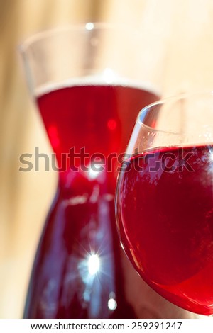 Glass of homemade red wine with carafe on stone wall background in rays of sunlight. Summertime outdoors close-up.