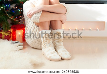 Young girl arms hugging legs in cozy warm woolen ornamental socks with pompons. Indoors.