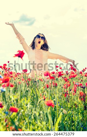 Carefree funny girl singing in poppy flowers field. Summertime outdoors.