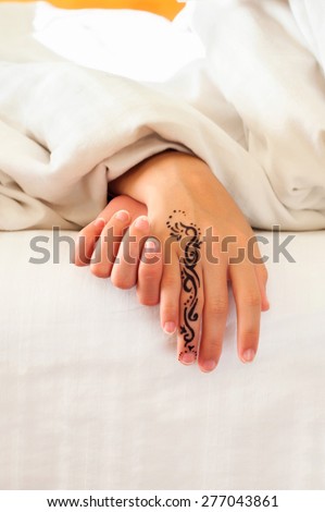 Little sleeping child hands with tattoo on white bed linen. Indoors closeup.