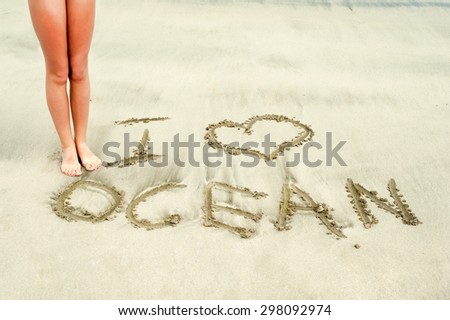 Young teenage girl slim legs and feet near I love ocean message handwritten in wet sand of Atlantic ocean. Summertime outdoors image.