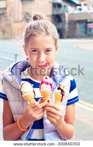 Happy smiling young girl holding many ice-cream with sweet sauces. Multicolored summertime outdoors image with instagram filter.