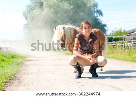 Friendship and trusting. Smiling teenage girl sitting near cute little shetland pony. Summertime outdoors image.