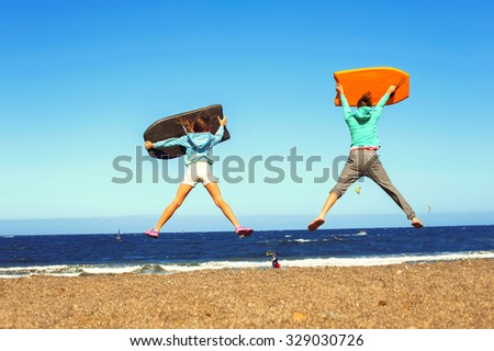 Little surfers. Two jumping kids excitement on windy beach of Atlantic ocean. Canary islands, Tenerife, Spain. Summertime vibrant outdoors horizontal image.
