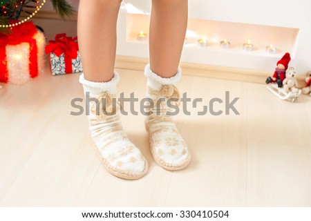 Young girl legs in cozy warm woolen ornamental socks with pompons on christmas background. Indoors horizontal image.