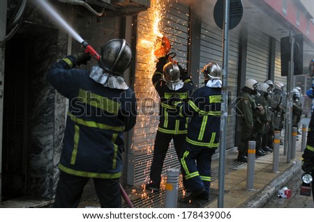 ATHENS-GREECE - DEC. 20. Fire fighters, protected by riot police, tries to extinguish burning store named \