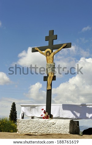 The image of the crucified Jesus on a wooden cross mounted on a marble base decorated with a few spring flowers.