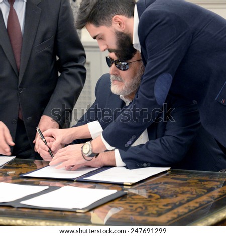 Greece,Athens, Jan. 27, 2015. New Greek Health Minister Panagiotis Kouroublis, who is blind, helped by his assistant to sign a protocol after a swearing in ceremony at the Presidential Palace.