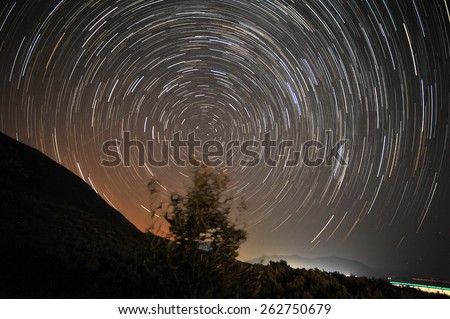 Star trails around the polar star as seen from coast line with olive trees in Central Greece.