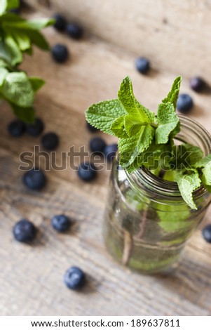 A mint in the cupping-glass with blueberries on the wooden table