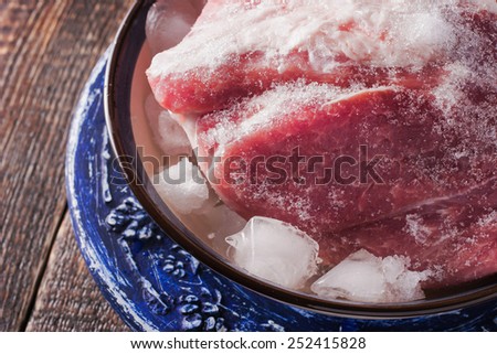 Frozen pork on the blue ceramic plate on the wooden table horizontal