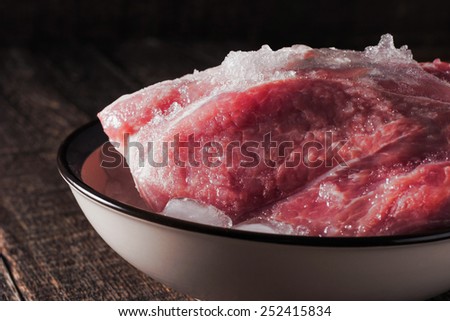 Frozen pork on the plate with ice on the wooden table horizontal